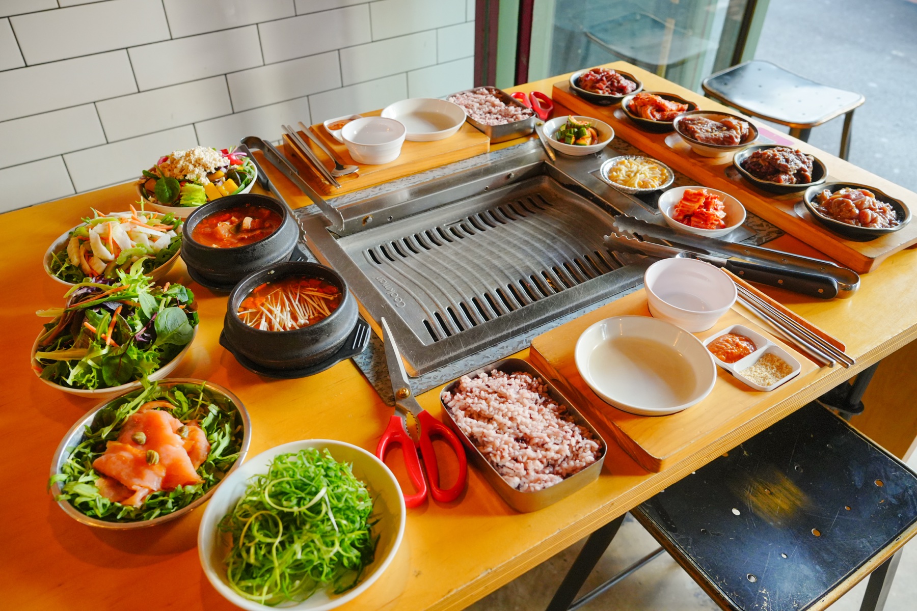 A full Korean BBQ table with a rectangular grill, meats, rice and side dishes